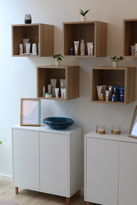 Foto af indretningen i den hyggelige kosmetiske klinik NordiQlinik i Kolding. Der er hudplejeprodukter på hylderne og små lys.