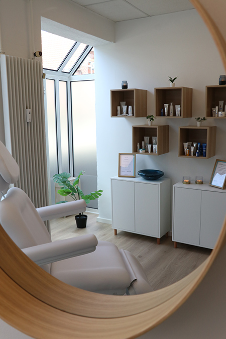 Billedet viser et spejl, som gengiver indretningen i kosmetisk klinik NordiQlinik i Kolding. Der er en behagelig stol og mange hudplejeprodukter.